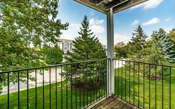 A balcony with a black railing and a view of a tree and a building.